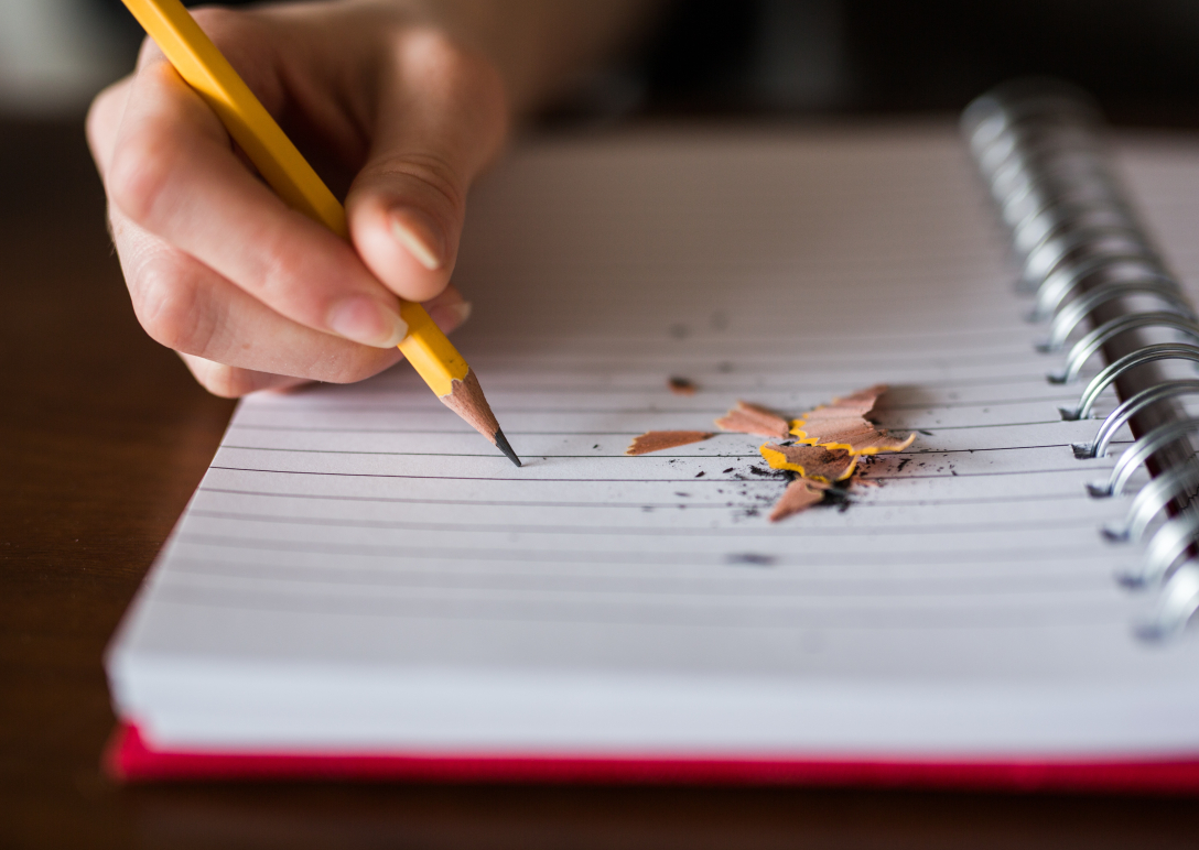 an image of a notebook. Someone is writing on the page and there are pencil shavings next to the pencil.